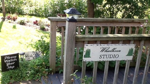Ein hölzernes Tor mit einem Schild, auf dem 'Wheelhouse Studio' steht, und einem weiteren Schild mit der Aufschrift 'Bitte vorsichtig'.