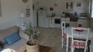 A cozy living room with a sofa, a dining table with chairs, a kitchen area with appliances, and a clock on the wall. - Charming rentals (Mazan)