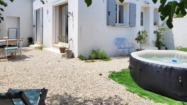A white building with blue shutters, a small patio with a table and chairs, and a hot tub. - Charming rentals (Mazan)