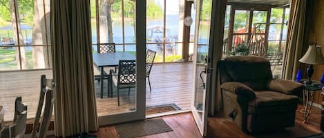 A cozy living room with a wooden floor, a large window, and a view of a deck and outdoor furniture.
