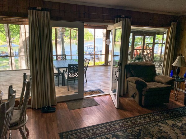 Una sala de estar acogedora con piso de madera, un ventanal y vistas a una terraza con mobiliario exterior.