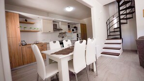 A modern kitchen with white cabinets, a dining table with white chairs, and a black spiral staircase. - CASA VACANZE CALIPSO (Scario)
