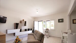A modern living room with a sofa, a dining table with chairs, a flat-screen TV mounted on the wall, and a window providing natural light. - CASA VACANZE CALIPSO (Scario)
