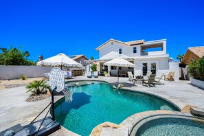 A residential property with a swimming pool, outdoor seating, and a two-story house.