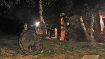 Un espacio al aire libre rústico con una gran rueda de metal, árboles y un muro de piedra.