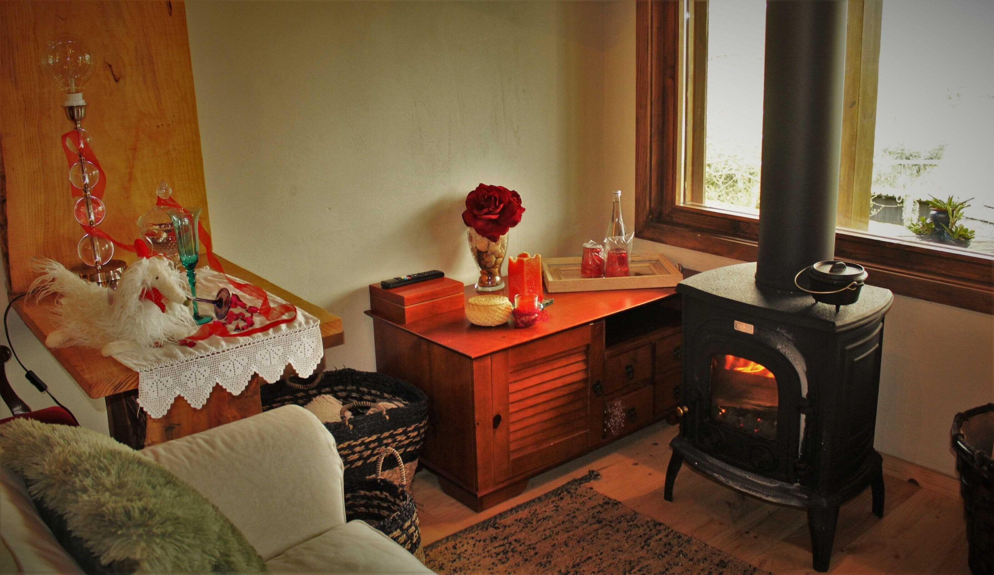 Un salon chaleureux avec une table en bois, un vase contenant une rose rouge, un meuble en bois et un poêle à bois.