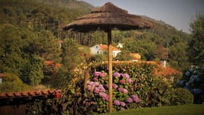 Ein mit Stroh gedecktes Gazebo, umgeben von üppigem Grün und blühenden Pflanzen.