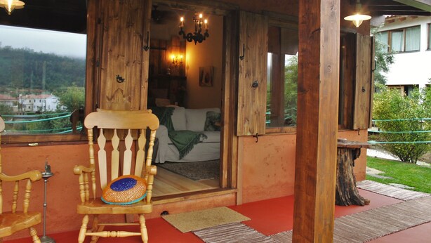 Ein hölzerner Schaukelstuhl mit Kissen, ein Holztisch und Blick auf ein Schlafzimmer mit Bett und einer Chandelier.
