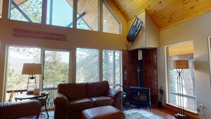 A cozy living room with a leather sofa, a fireplace, and large windows offering a view of the outdoors.