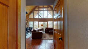 A spacious living area with a high ceiling, wooden beams, and large windows offering a view of the outdoors.