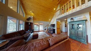 A spacious living room with a large brown leather sofa, a wooden ceiling, and a staircase leading to an upper level.