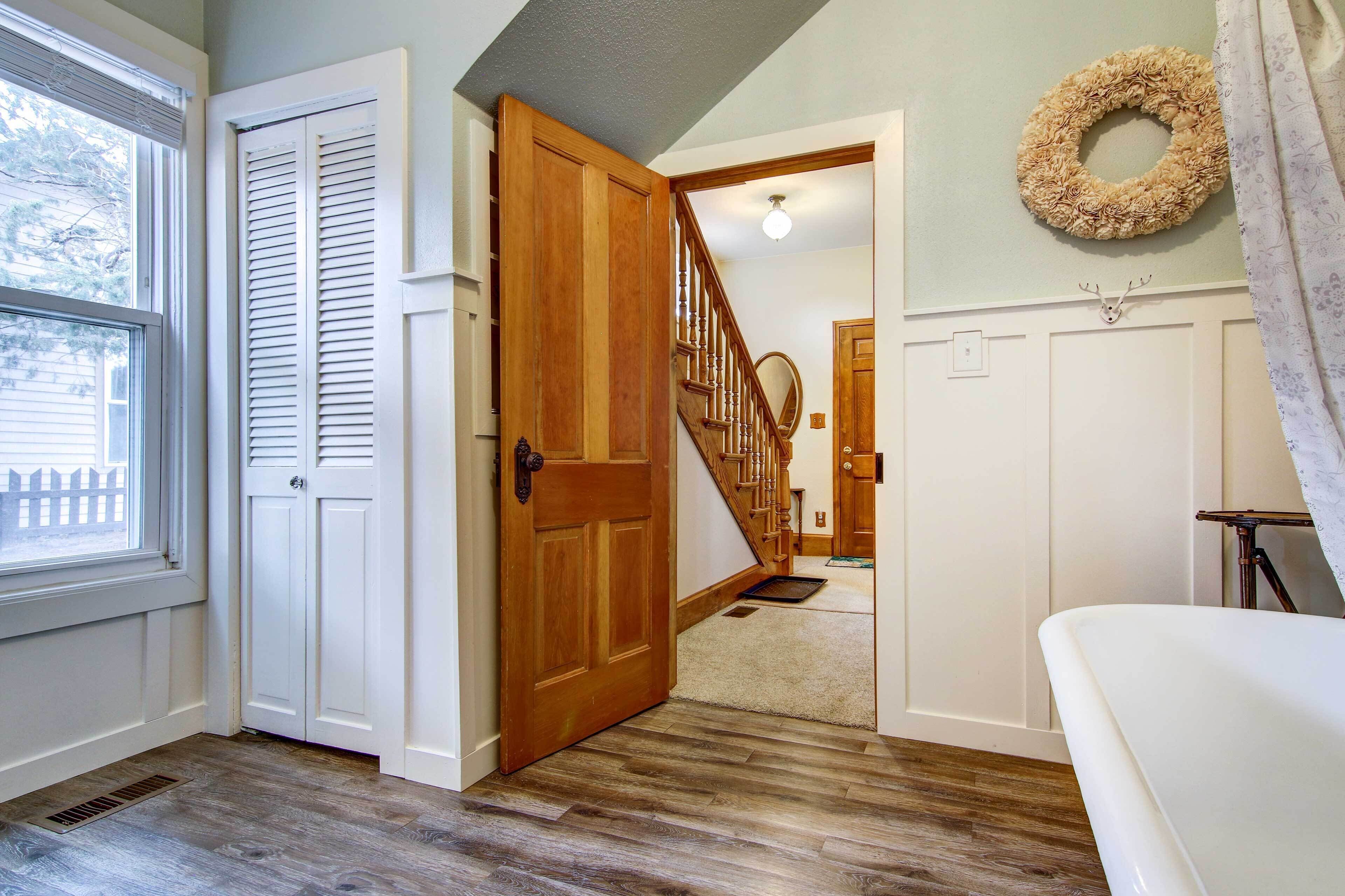 Un pasillo con puerta de madera, una escalera y un adorno colgante en la pared.
