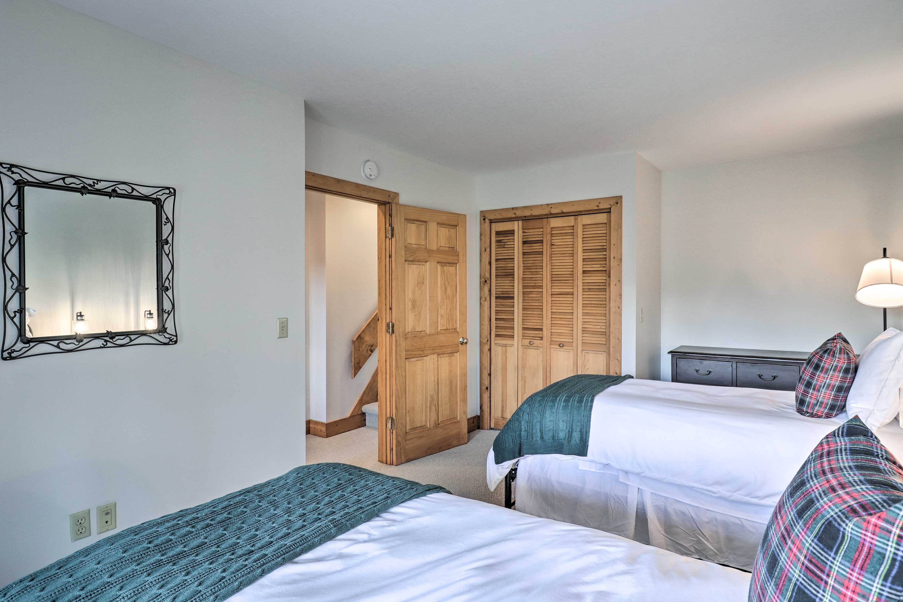 Habitación de hotel con dos camas, un armario de madera, un espejo y una escalera que conduce a otra habitación.