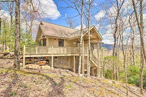 Une cabane à deux étages avec un balcon, entourée d’arbres et d’un paysage rocheux.
