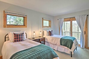 Une chambre avec deux lits, une table de chevet, une fenêtre avec des rideaux et une vue sur les arbres.
