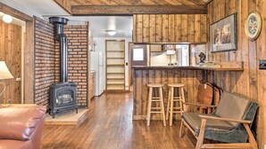 Um quarto aconchegante com parede de tijolos, teto de madeira, fogão preto, espaço de bar com banquetas e sofá de couro.