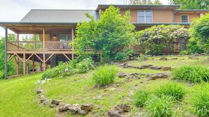 Una baita di legno con veranda e terrazza coperta, circondata da vegetazione lussureggiante e rocce.