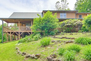 Een houten chalet met veranda en overdekt terras, omringd door weelderige begroeiing en rotsen.