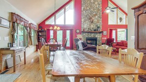 Un'ampia sala da pranzo con un grande tavolo in legno e sedie, un camino in pietra e vista all'esterno tramite ampie finestre.