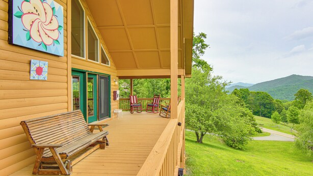 Un portico in legno con una panchina e poltrone a dondolo, un quadro e vista su un paesaggio verde.