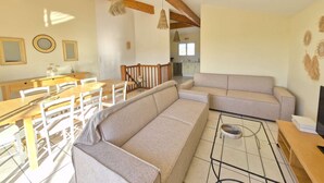 A spacious living area with a wooden dining table, beige sofa, and a kitchen in the background. - Beautiful twin villa of 100m² for 6 people (BISCARROSSE)