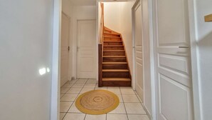 A hallway with a wooden staircase, white doors, and a yellow mat on the floor. - Beautiful twin villa of 100m² for 6 people (BISCARROSSE)
