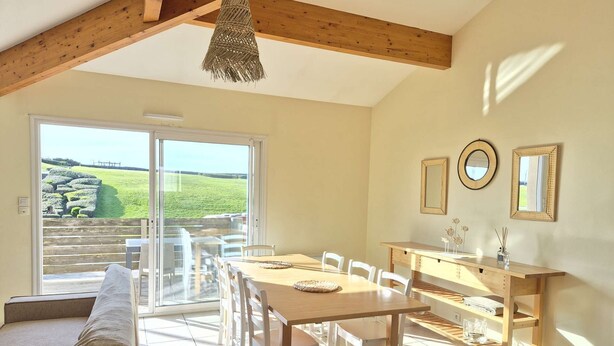 A dining area with a wooden table and chairs, a bench, and a view of a green landscape through a sliding glass door. - Beautiful twin villa of 100m² for 6 people (BISCARROSSE)