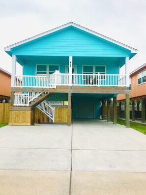 A two-story building with a balcony, a wooden fence, and a garage. - Flock On-Pet friendly beach house close to the beach, golf cart zone (Port Aransas)