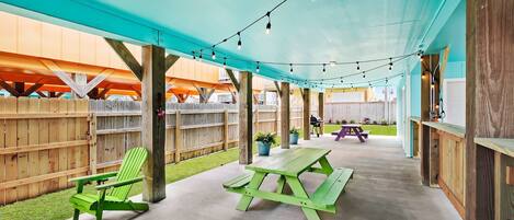 An outdoor patio area with a green Adirondack chair, a picnic table, and string lights.