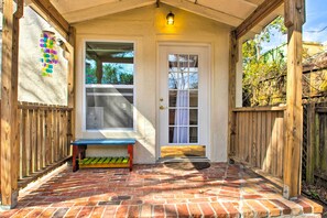 A covered porch with a brick floor, a wooden bench, a white door, and a window. - Colorful Pensacola Oasis: 1 Block to Bayview Park! (Pensacola)