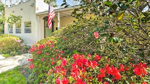 Un edificio con fachada blanca, una bandera y un jardín con flores rojas.