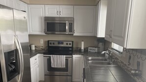 Una cucina moderna con elettrodomestici in acciaio inossidabile, mobili bianchi e pavimento piastrellato.