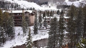 A lodge with multiple floors, surrounded by snow-covered trees and a ski slope in the background.