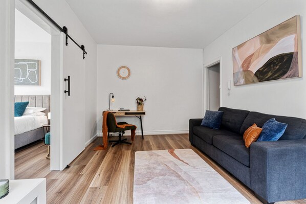 Una sala de estar moderna con un sofá gris, un escritorio de madera y una cama con almohada azul.