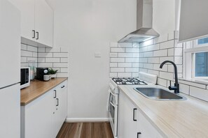 A compact kitchen with white cabinets, a wooden countertop, a gas stove, a sink, and a window.