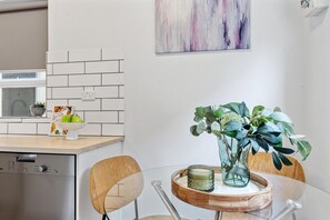 Una cocina moderna con salpicadero de azulejos blancos, encimera de madera, una mesa de comedor con sillas y un jarrón con hojas verdes.