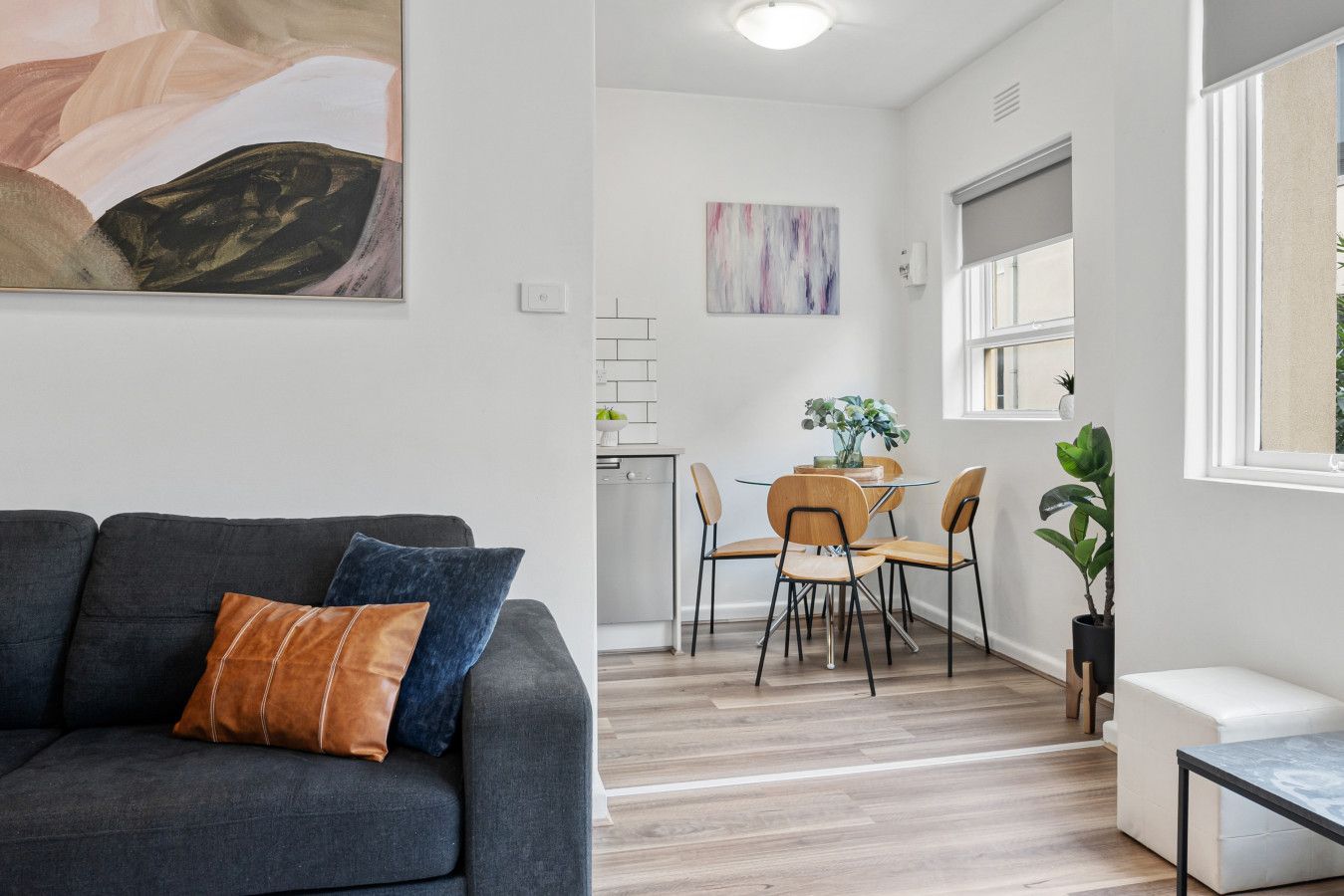 A modern living room with a grey sofa, a dining area with a round table and chairs, and a large window.