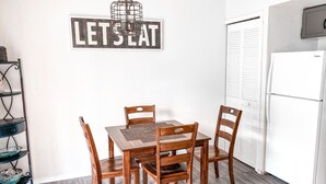 Un coin repas avec une table et des chaises en bois, un présentoir en métal contenant de la vaisselle et un réfrigérateur.