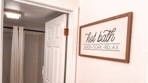Une salle de bain avec un rideau de douche, une porte et un panneau sur le mur indiquant : « Bain chaud, LAVER, SE DÉTENDRE. »