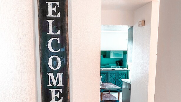Un couloir avec une pancarte « BIENVENUE », une petite table et une vue sur un coin cuisine.