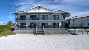 A multi-story beachfront hotel with balconies, a sandy beach in front, and a clear sky.