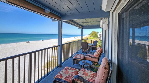 A covered balcony with wicker furniture and a view of the beach.