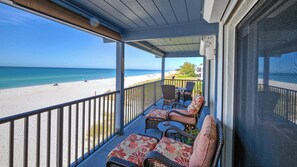 Een overdekt balkon met rieten meubilair en uitzicht op het strand.