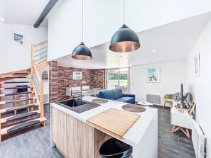 Une cuisine moderne avec un îlot central, un escalier en bois et un coin repas agrémenté d’un canapé bleu.