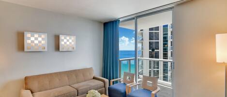 Een hotelkamer met een bank, twee fauteuils, een bijzettafeltje en uitzicht op de oceaan.