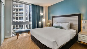 Moderni hotellihuone, jossa on suuri sänky, penkki, yöpöytä, lamppu ja näkymä korkeaan kerrostaloon.