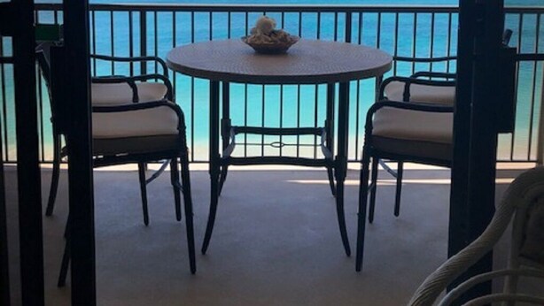 A balcony with a round table and two chairs, overlooking a clear blue sea and distant land. - Hawaiian Prinicess one bedroom
1990/NUC-2240 (Waianae)
