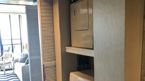 A laundry room with a washing machine and dryer, a wooden ceiling, and a view of a living area with a couch and striped rug. - Hawaiian Prinicess one bedroom
1990/NUC-2240 (Waianae)
