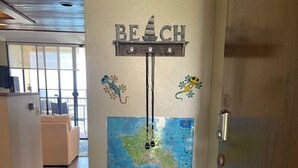 A corner of a room with a white console table, a wall-mounted map, and a 'BEACH' sign above it. - Hawaiian Prinicess one bedroom
1990/NUC-2240 (Waianae)
