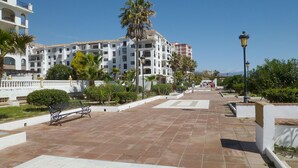 A paved walkway with benches, palm trees, and a building with balconies. - One bedroom on the ground floor (Manilva)